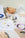 Assorted pastel desk items, packaging, a woven bowl, color swatches, and sketches arranged on a white surface.