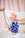 A hand places a pink flower in a blue vase with hand designs, while another hand holds a white cloth backdrop.