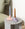 Two twisted candles, one blue and one brown, in pastel pink and purple holders on a round gray side table.
