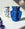 Two vases with abstract face designs, one white and one blue, sit on a surface with flowers and shadows nearby.