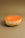The Octaevo Melon Candle, shaped like half a cantaloupe, sits on a plain light brown tabletop.