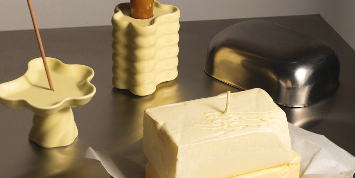A block of butter on its on a metallic surface, surrounded by yellow ceramic dishes and a metallic butter dish.