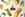 Assorted food- and drink-themed ornaments, including a lemon, cherries, peas, a cannoli, drink bottles, a glass with ice, and a red onion, arranged on a light background.