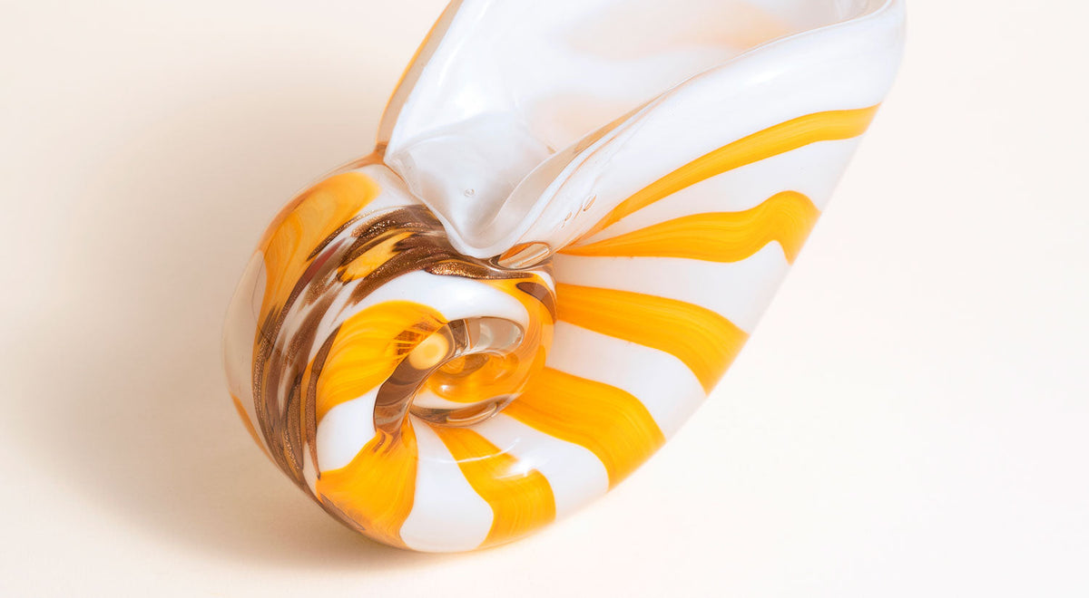 Close-up of a glass sculpture shaped like a seashell, with swirling green tones at the tip and orange accents on the body