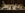 A festive dinner table set for four with elegant white dishes, two lit candles, sparkling drinks, a small cake, pastries, bread, butter, and decorative holiday accents.