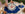 A person holds a decorative plate with blue and red designs and French text, above a blue placemat on a table set with eggs, bread, whipped cream, and a croissant outdoors.