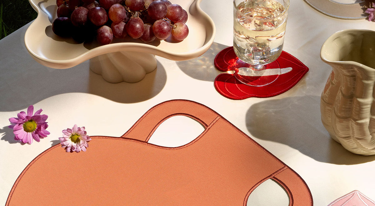 A table setting with ocean-themed plates, a blue and red placemat, shell-shaped cutlery and sea-inspired coasters.