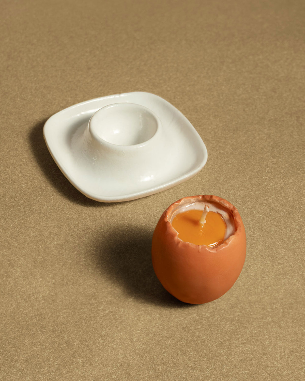 The OCTAEVO Soft-Boiled Egg Candle, shaped like an egg in an eggshell, rests by a white ceramic egg cup.