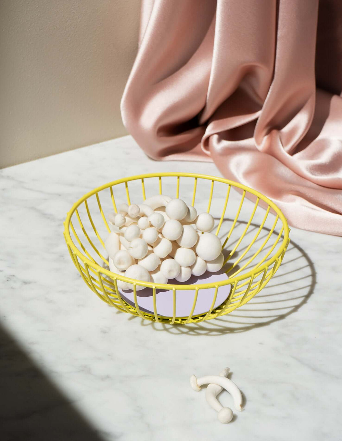 A yellow wire basket with white mushrooms on a marble surface, with a pink satin cloth in the background.