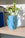 A Domus Mini Paper Vase by OCTAEVO with fresh flowers sits on a light wooden shelf in sunlight.