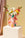 A pink OCTAEVO paper vase decorated with colorful hand illustrations, filled with flowers, displayed on a pedestal.