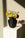 The Lido Mini Paper Vase by OCTAEVO features a yellow grid and casts an elegant shadow on a sunlit pedestal.