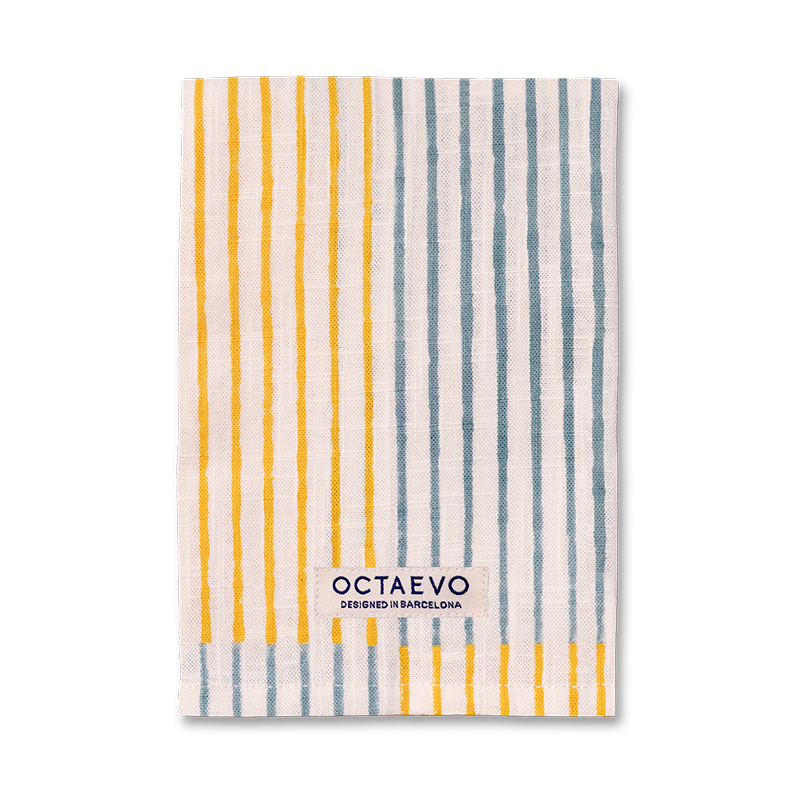 Un paño de cocina de lino rectangular con rayas verticales naranjas sobre un fondo blanco roto, con el nombre de la marca 'OCTAEVO' impreso cerca de la parte inferior.