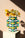 Yellow flowers in the OCTAEVO Artesania Paper Vase with teal, yellow, and black patterns on a white pedestal in sunlight.