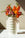 The Coral Paper Vase by OCTAEVO holds pink and orange snapdragons on a sunlit marble surface.