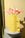 OCTAEVO's Dendra Paper Vase in yellow with pink anthuriums and a pear on a gray pedestal, beige background.