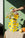 A hand arranges flowers in the OCTAEVO Nazar Paper Vase with eye motifs, on a sunny table with oranges.
