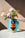 A light blue OCTAEVO Paper Vase with a colorful geometric stacked-figurine design, filled with white and pink flowers. A person's hand is adjusting the flowers.
