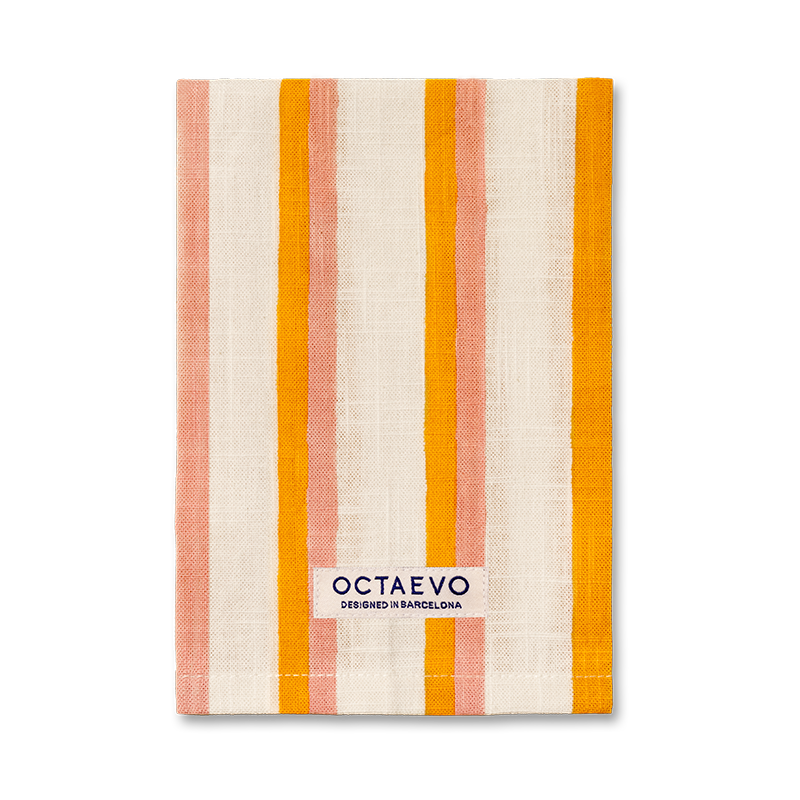 Eine rechteckige Serviette mit senkrechten Streifen in Orange, Rosa und Creme, mit einem Markenetikett am unteren Rand mit der Aufschrift 'OCTAEVO DESIGNED IN BARCELONA'.