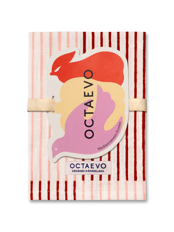 Una servilleta de Octaevo con un patrón de rayas rosas y rojas, sujeta con una banda elástica beige y con una gran pegatina multicolor en la parte frontal.