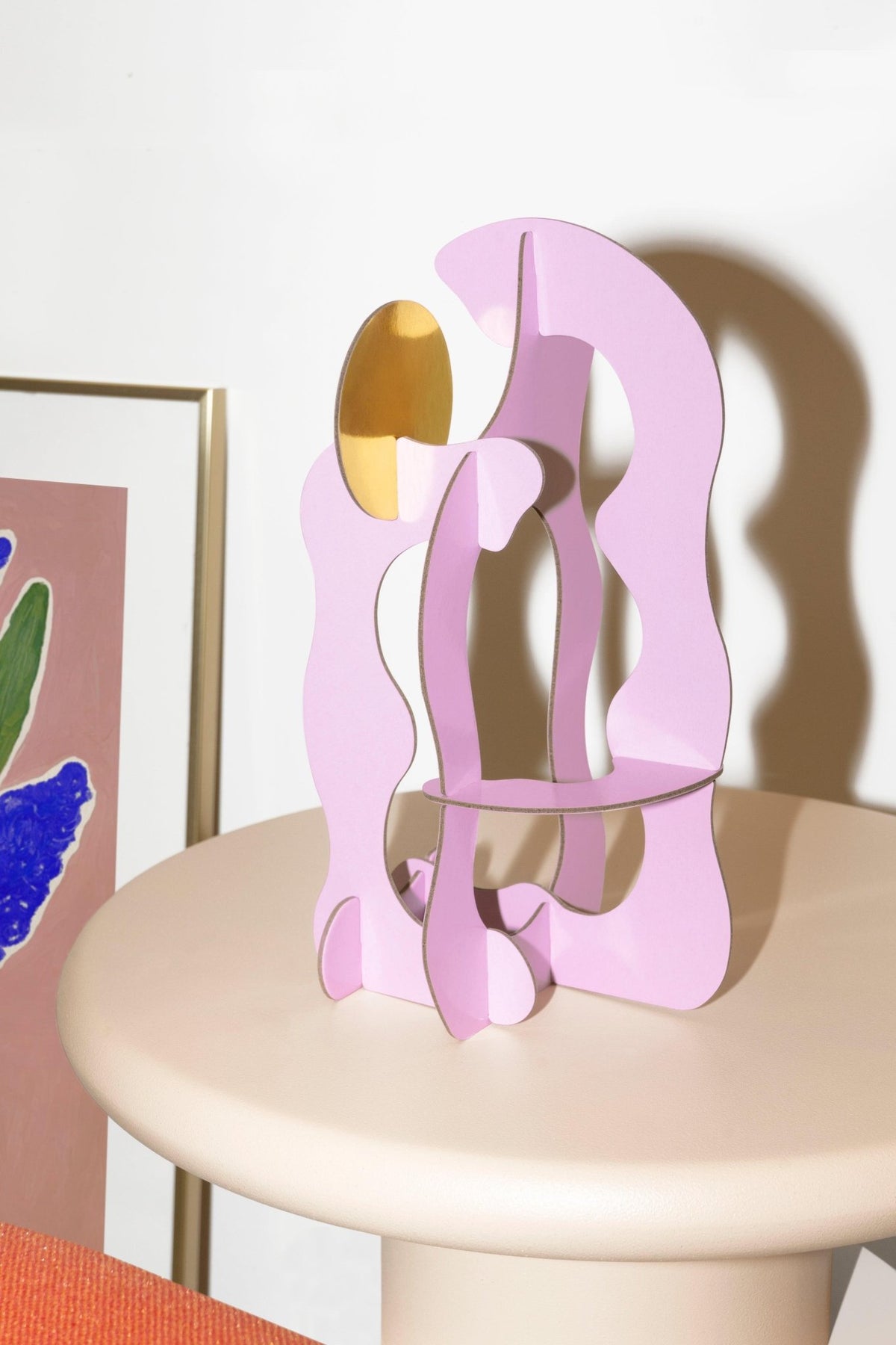 Air Paper Sculpture by Octaevo—a pink and gold decor piece on a table with colorful framed art in the background.