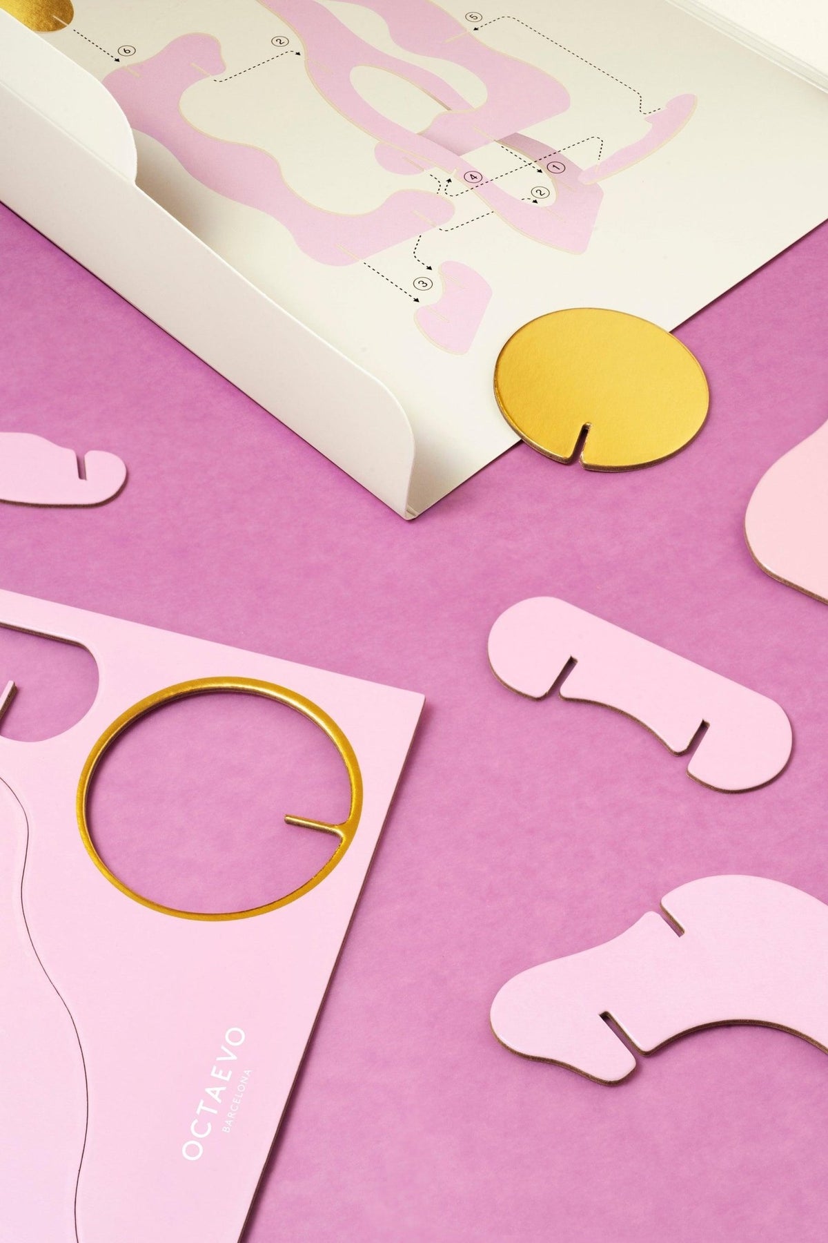 Flat lay of Octaevos Air Paper Sculpture, pink and gold abstract pieces with card and white envelope, perfect decor.