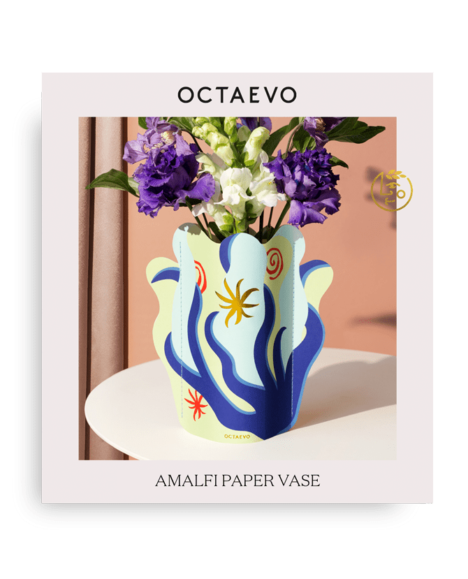 Le mini vase en papier Amalfi d'Octaevo, garni de fleurs violettes et blanches, se dresse sur une table blanche.