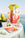 The Octaevo Amalfi Paper Vase features yellow flowers, fruit, and a drink on a white tablecloth by the Amalfi Coast.