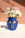 The Apolino Mini Paper Vase by OCTAEVO, with a yellow abstract face, holds blooms on a white surface and peach background.