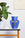 The OCTAEVO Apollo Paper Vase with a face design sits on a table beside a potted plant and white decor.