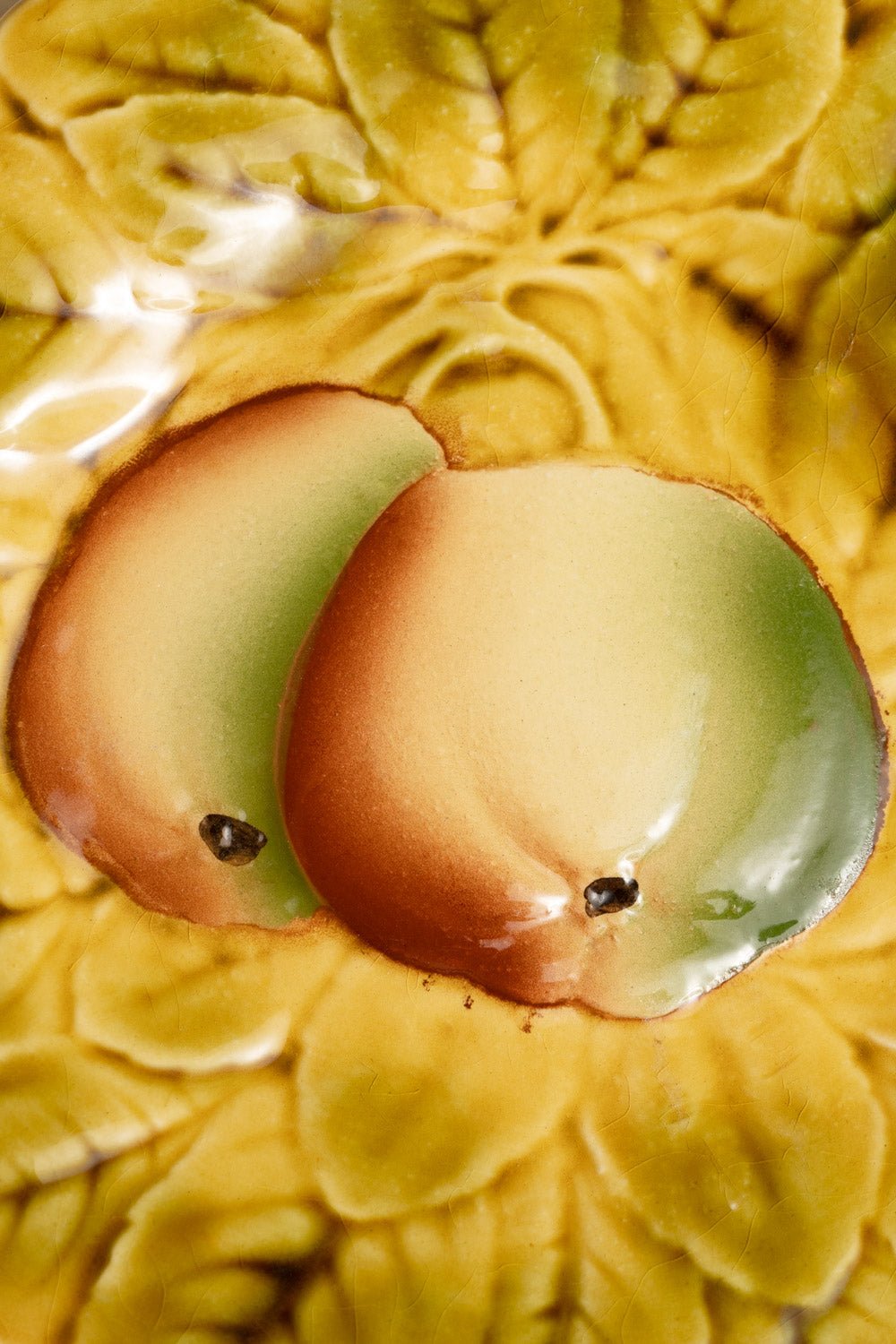 Two apples with green and red hues sit on the yellow, leafy Apple Majolica Plate by OCTAEVO.