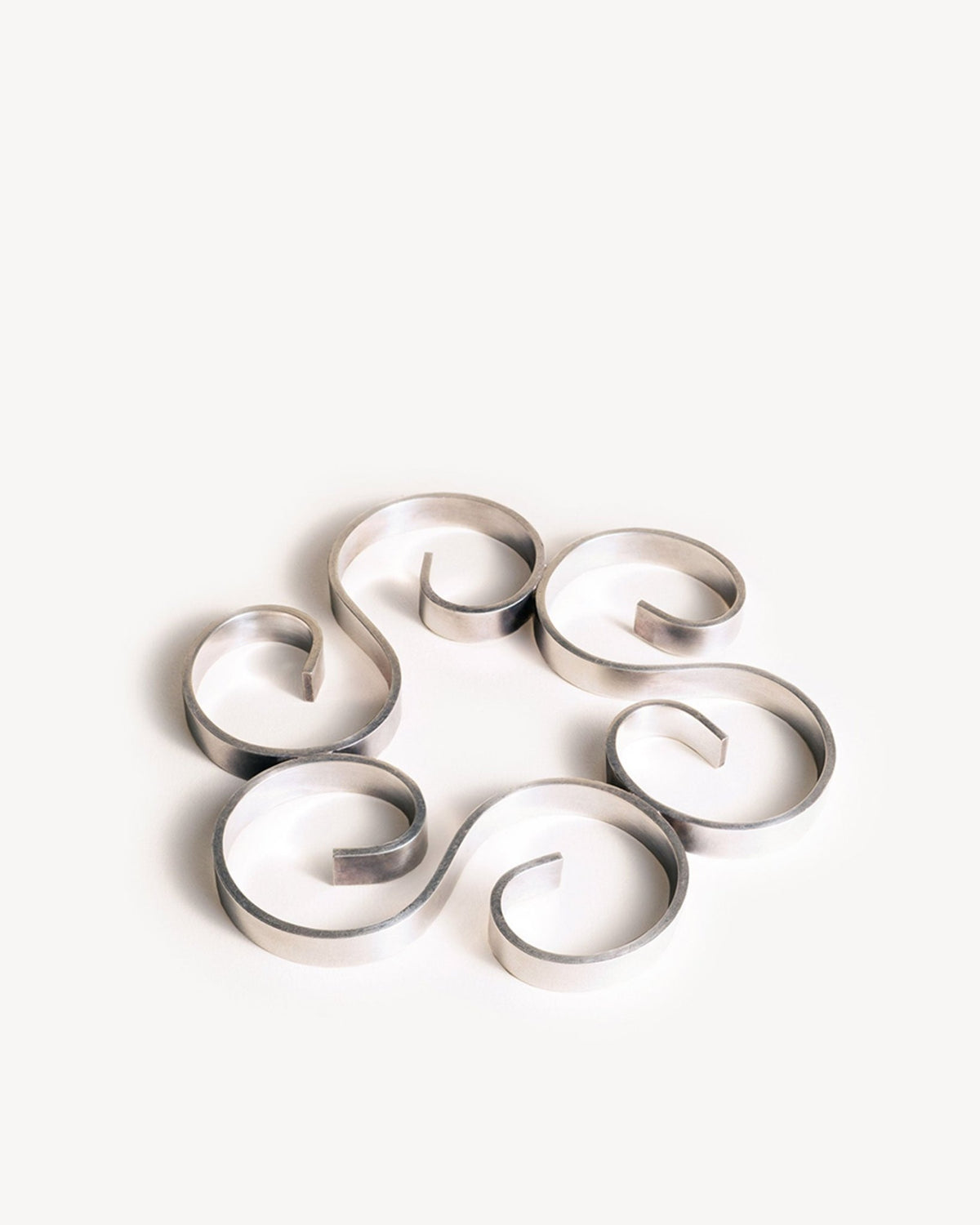 Six silver strips form spirals on the OCTAEVO Arabesque Silver Trivet, inspired by French design elegance.