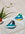 Two OCTAEVO Atlas Glass Birds are displayed on a light surface near greenery in bright natural light.