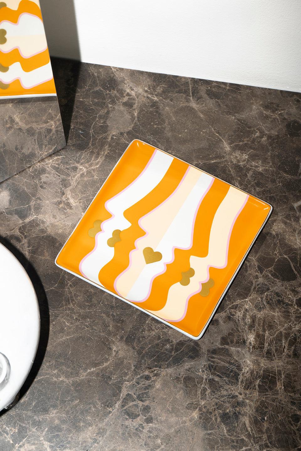 A stylish gift, the orange Beso Ceramic Tray features face profiles and gold hearts to elevate your table decor.