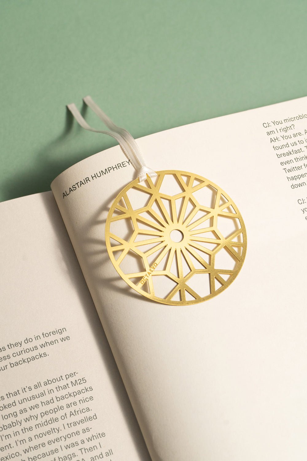 The OCTAEVO Bookmark Christmas Bauble rests on an open book like a holiday ornament against a green background.