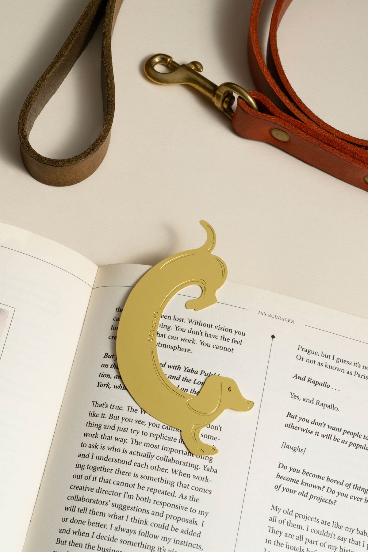 Le marque-page Teckel OCTAEVO—un compagnon en laiton plein de fantaisie—repose sur un livre ouvert avec sa lanière en cuir et son fermoir.