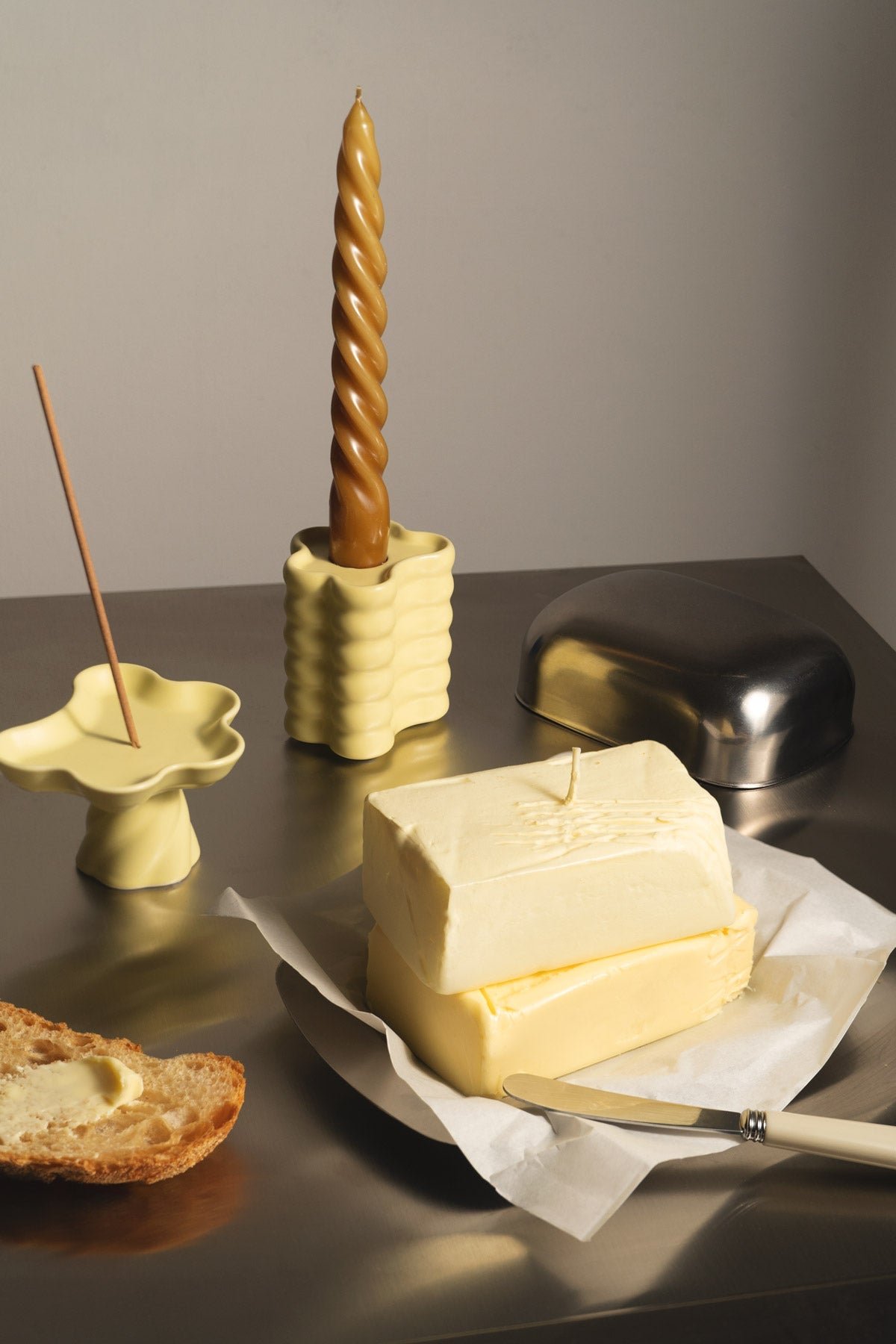 Two stacked sticks of butter, toast, knife, and OCTAEVO Butter Candle on a metallic surface.