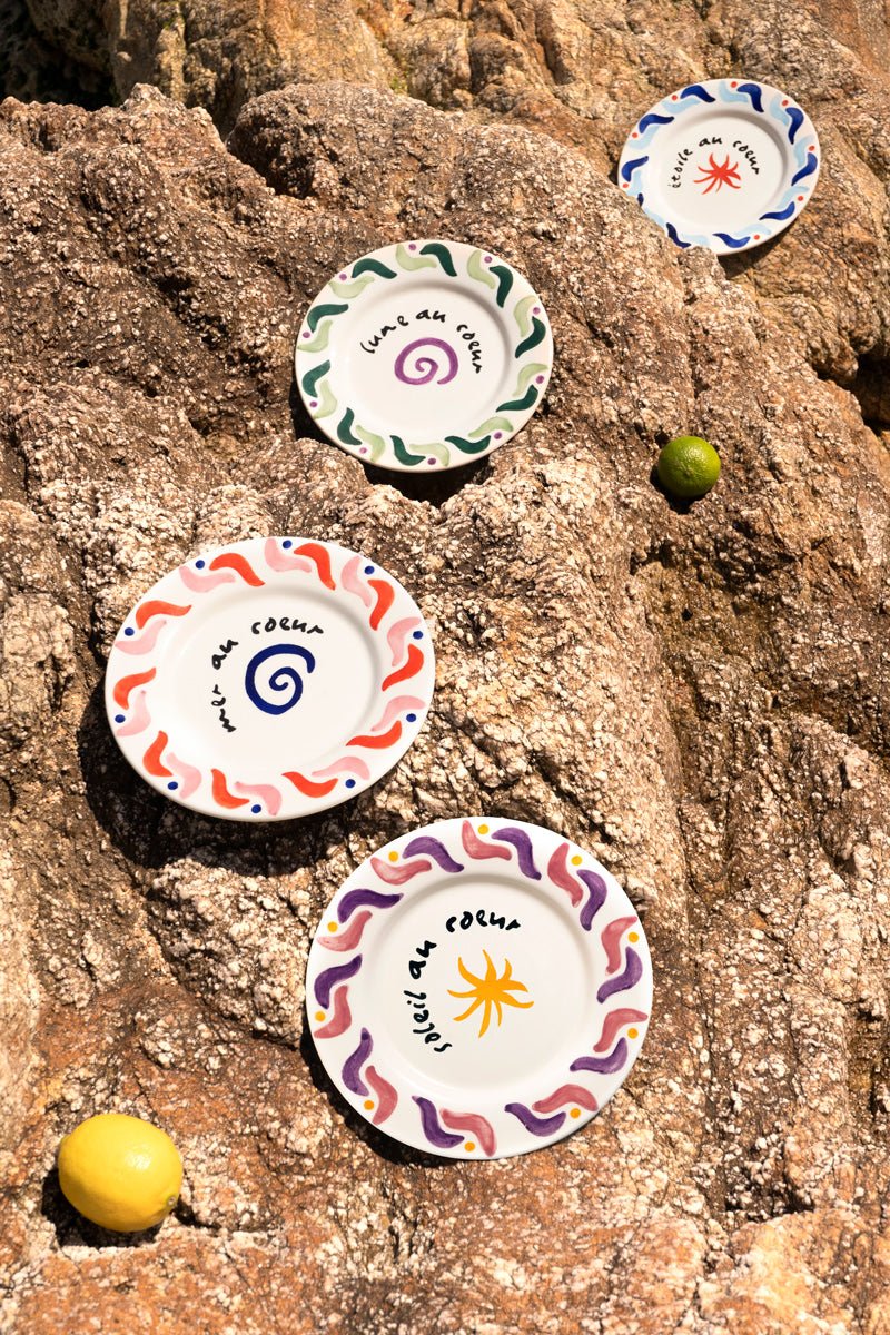 Four Octaevo Cala Secreta Plates with colorful patterns sit on rocks, with a lemon and two limes nearby.