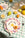 A colorful table with fruit, cutlery, and Octaevo’s hand-painted Cala Secreta Plate on a checkered cloth.