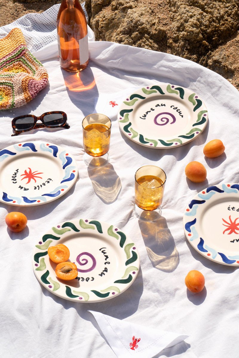 A summer picnic with Octaevo Cala Secreta plates, amber glasses, apricots, sunglasses, and rosé on white cloth.