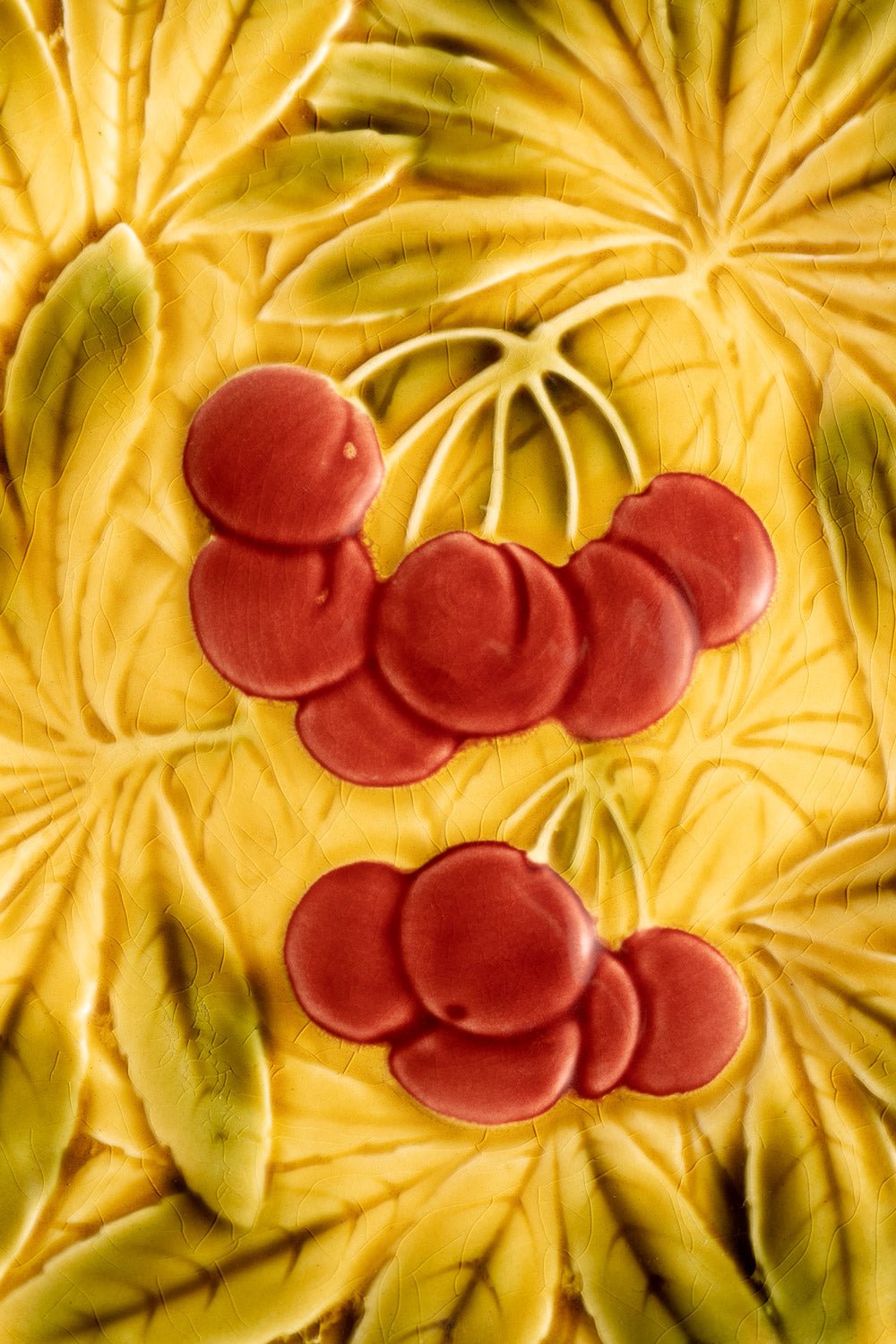 Red cherries with green stems on OCTAEVO’s Cherry Majolica Plate with an Art Nouveau ceramic relief pattern.