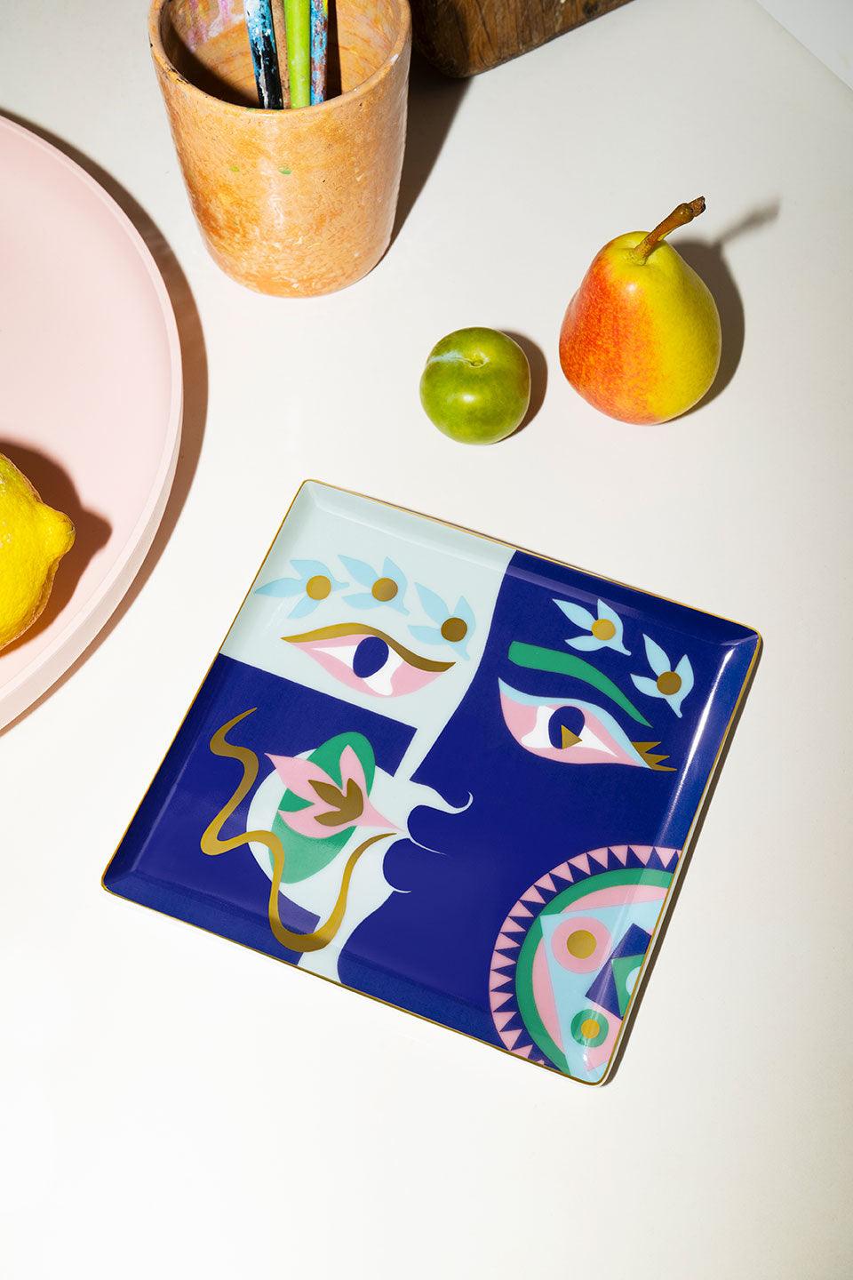 The Octaevo Claire Johnson Ceramic Tray - Blue features abstract face art and gold foil accents.