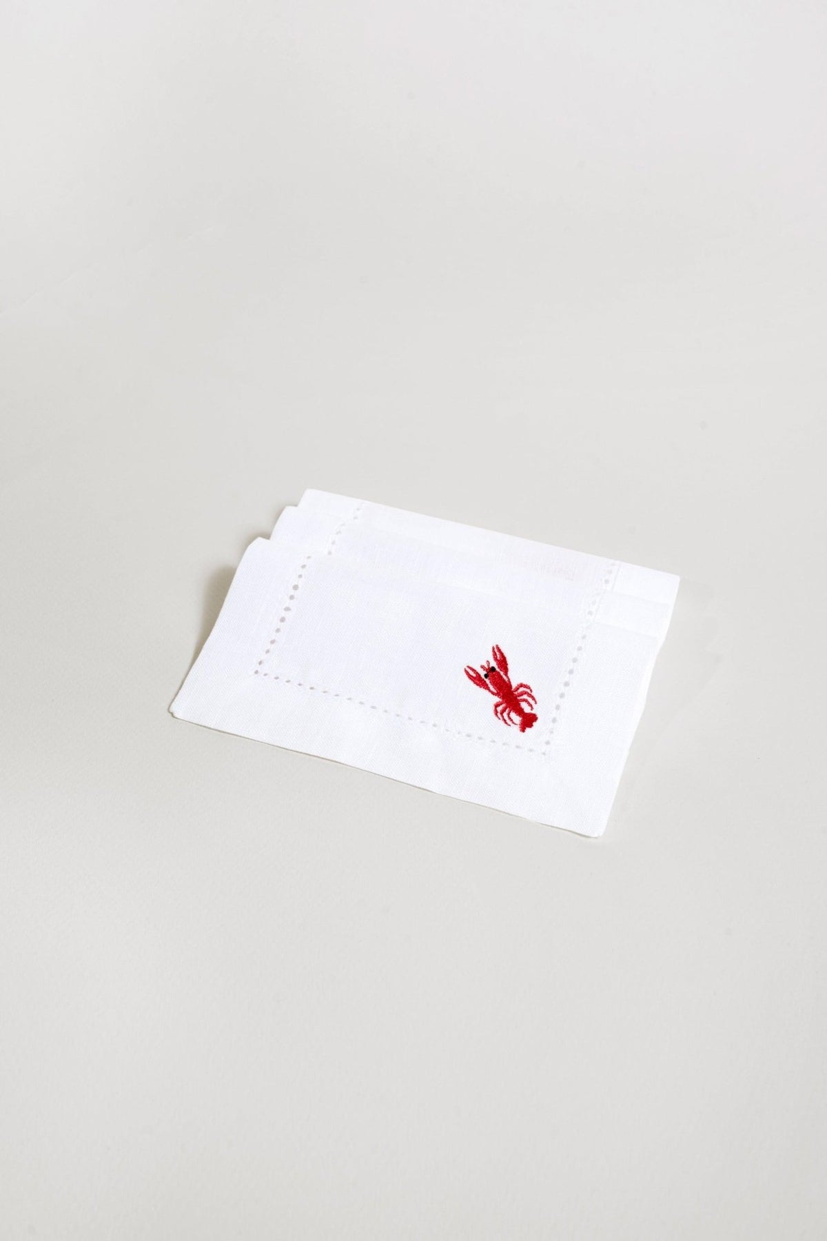 Les serviettes de cocktail Homard d'OCTAEVO (lot de 2)—des serviettes en lin écologiques et réutilisables, brodées d'un homard rouge.