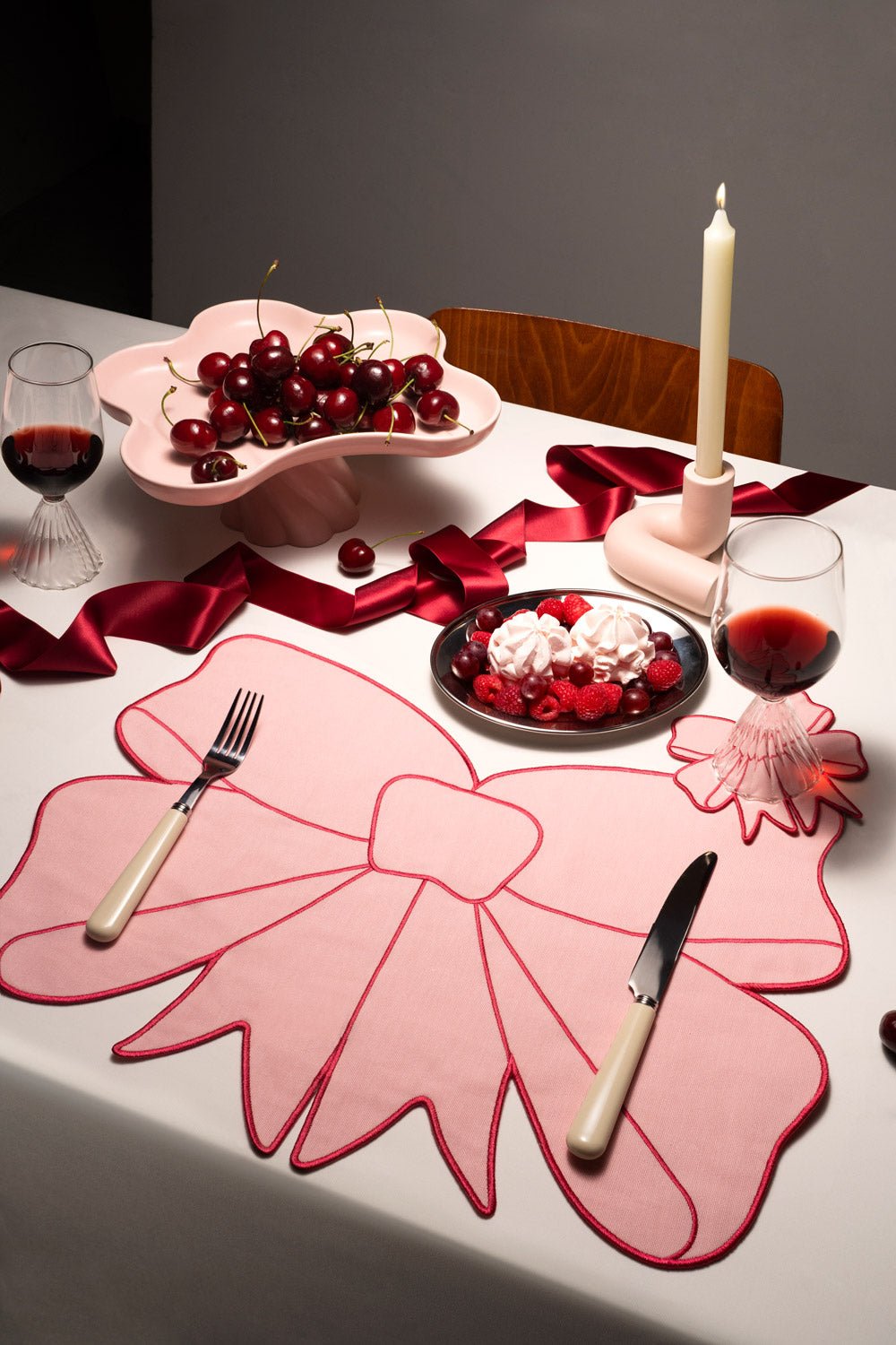 Une table dressée avec des dessous de verre Coquette OCTAEVO, un set de table à nœud rose, une décoration élégante, des cerises, des desserts et des verres à vin.