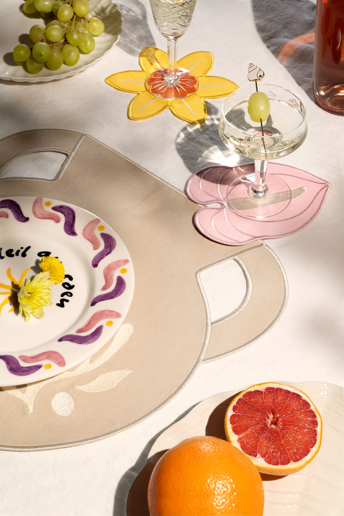 Les dessous de verre Jonquille d'OCTAEVO (lot de 4) sur un set de table tote bag, avec des fruits et des cocktails en plein soleil.