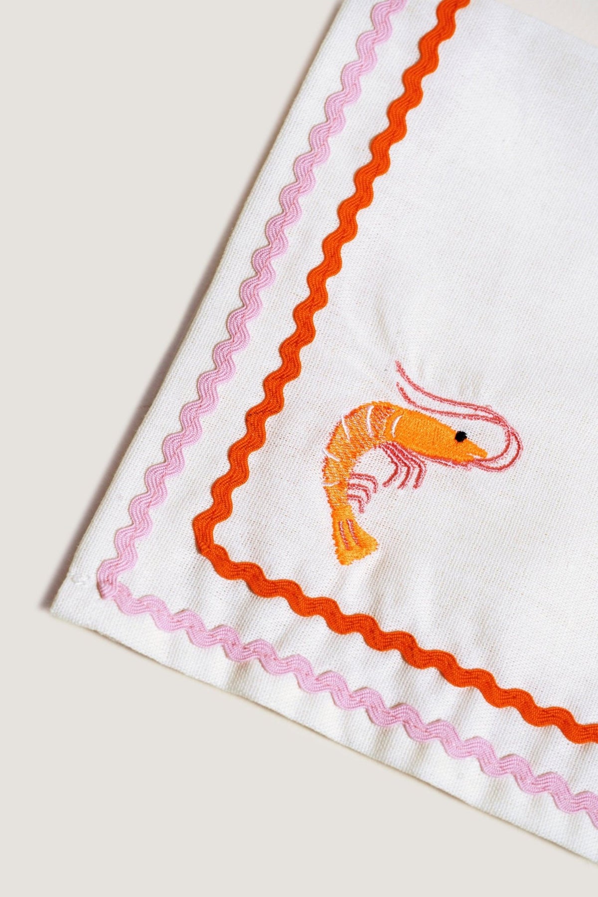 Octaevo Dinner Napkin Prawn (Set of 2): White linen with pink/orange trim and embroidered orange prawn in the corner.