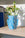 A Domus Mini Paper Vase by OCTAEVO with fresh flowers sits on a light wooden shelf in sunlight.