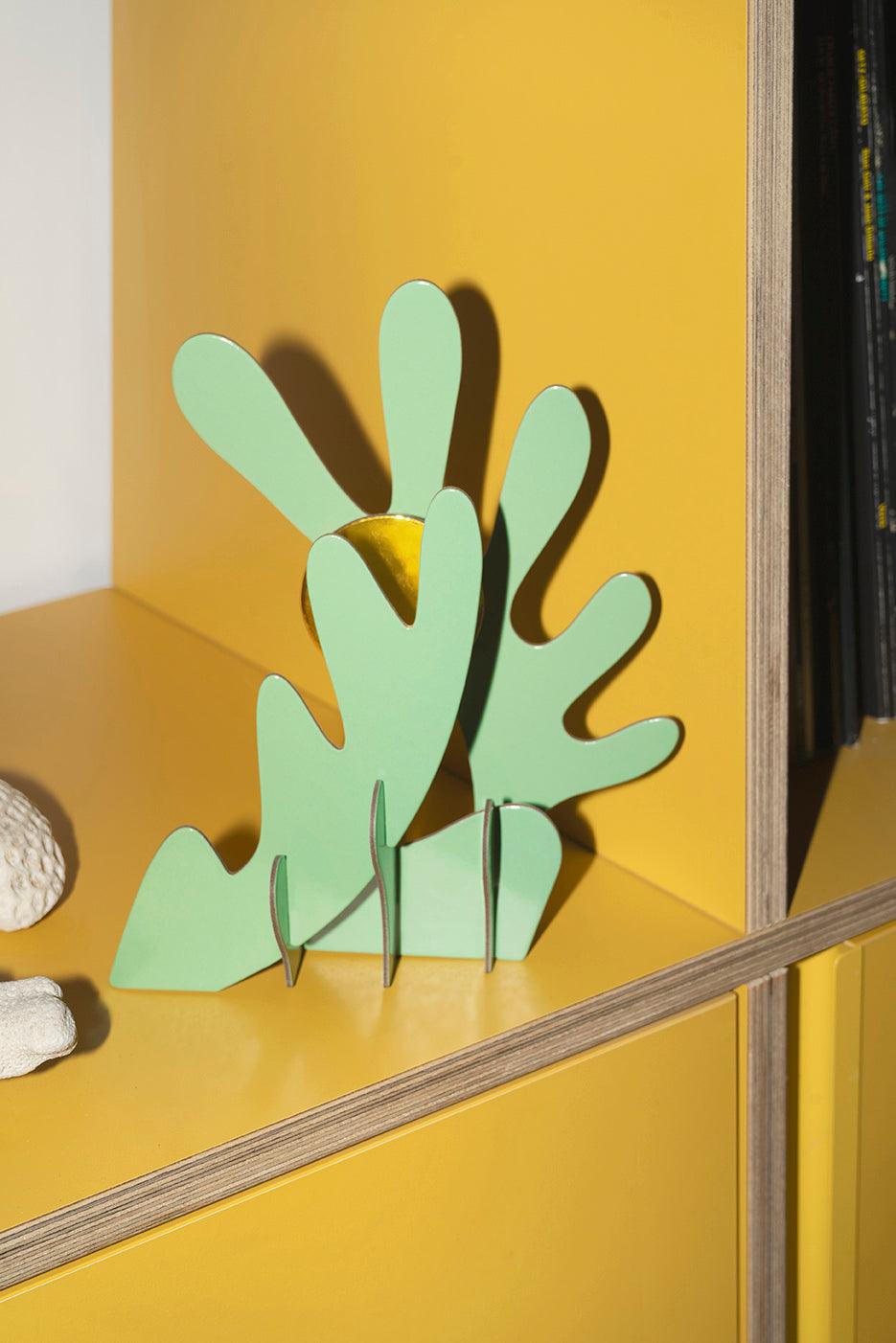 Octaevo Earth Paper Sculpture—green abstract decor with curves, displayed on a yellow shelf beside books and a white object.