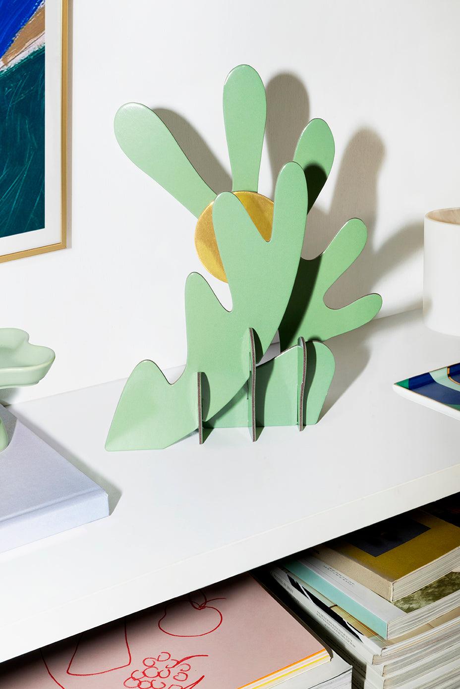 The Earth Paper Sculpture by Octaevo is a green cactus-shaped decor made of recycled cardboard with a golden sun accent.