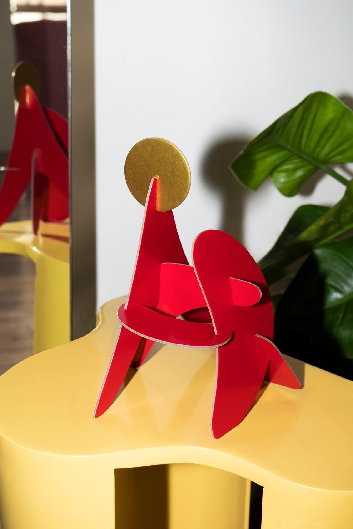 The Fire Paper Sculpture by Octaevo: a red and gold recycled cardboard decor piece on a yellow table with plant and mirror.